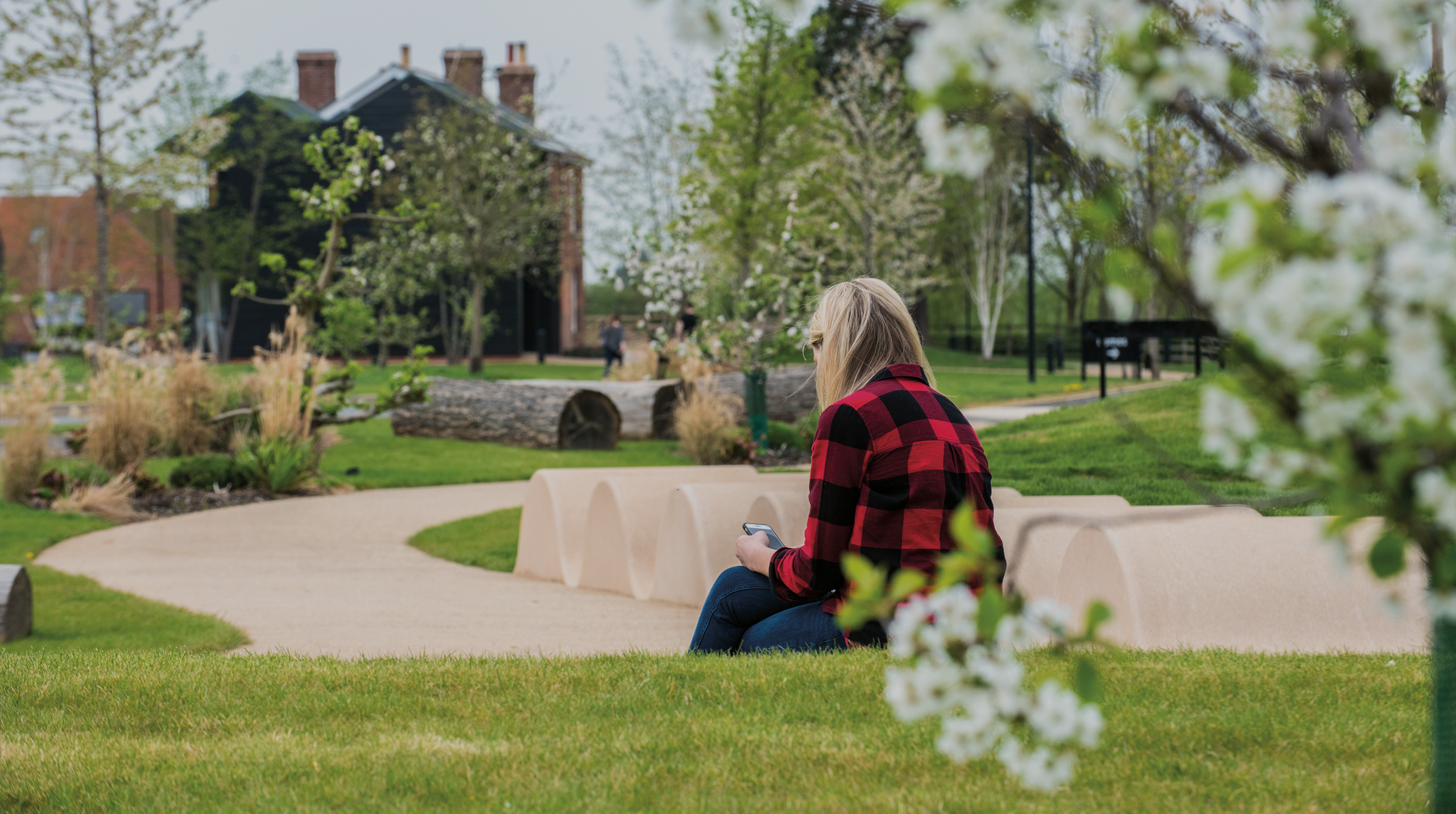 An adult sat in a park setting surrounded by greenery and blossoming trees.
