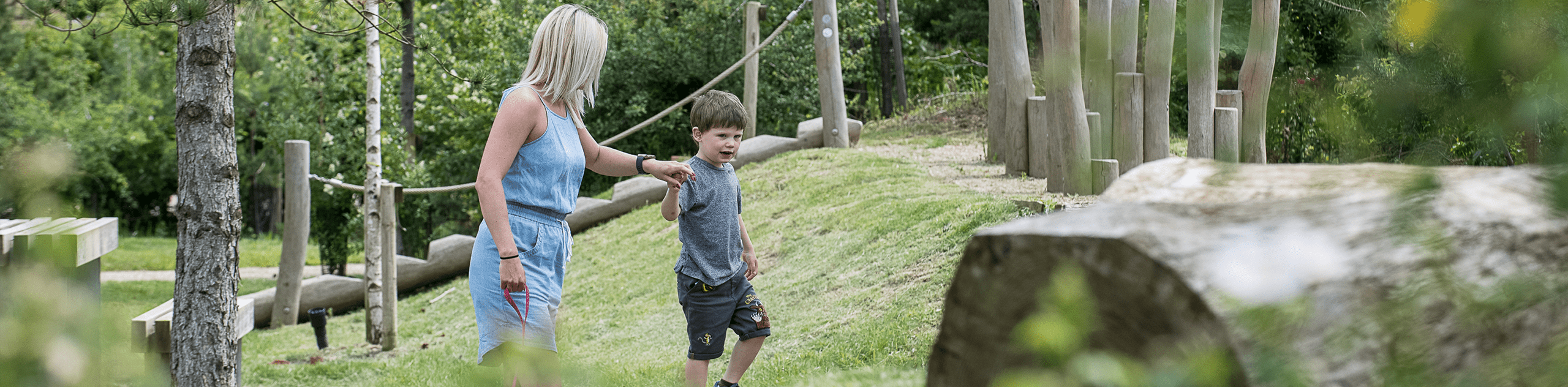 A photograph of a woman guiding her son through the landscape play elements along a green corridor. © BMD