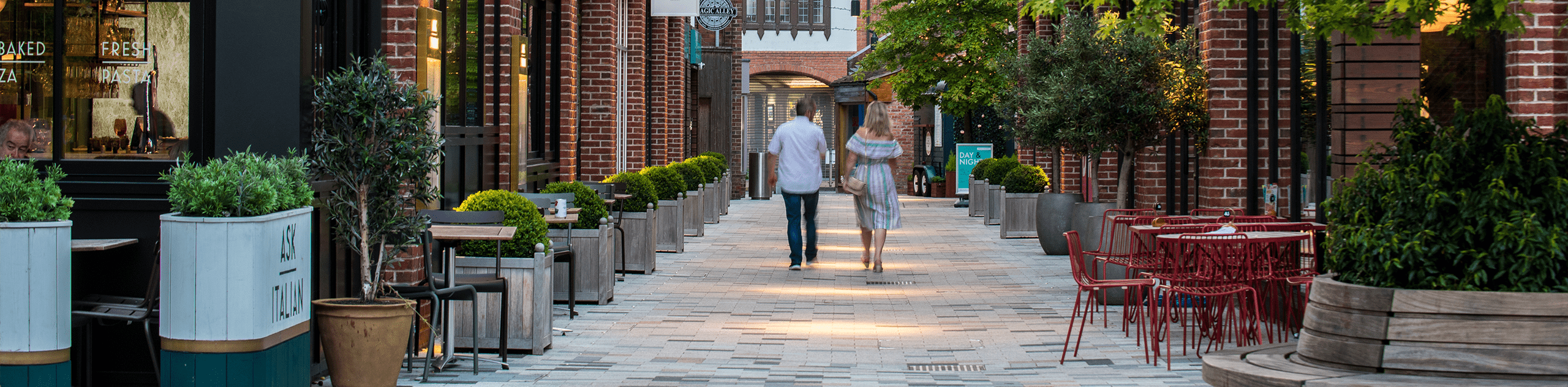 Photograph of couple walking through bell court, featuring resturant spill-out seating and trees in planters. © BMD Photograph of couple walking through bell court, featuring resturant spill-out seating and trees in planters. © BMD