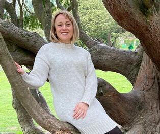 A photograph of a BMD employee sat on a low tree branch A photograph of a BMD employee sat on a low tree branch