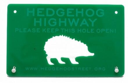 A Green sign with a white hedgehog silhouette on it, the text on the sign says hedgehog highway, please keep this hole open A Green sign with a white hedgehog silhouette on it, the text on the sign says hedgehog highway, please keep this hole open