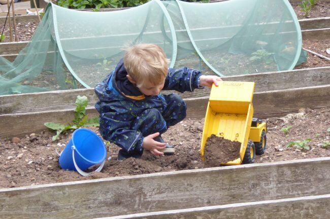 A child playing with a digger toy in an allotment 