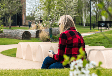 An adult sat in a park setting surrounded by greenery and blossoming trees.