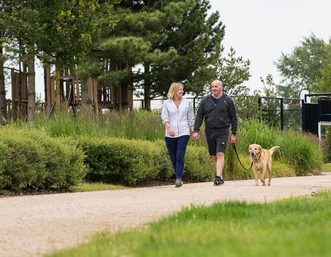 A photograph of a couple walking their dog through a local green space at Alconbury Weald