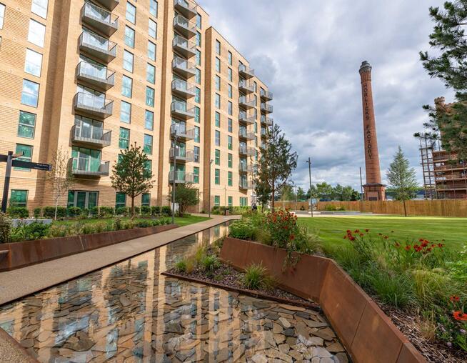 A photograph of apartment blocks within park setting including water features, planting and historic chimney in the background. © BMD