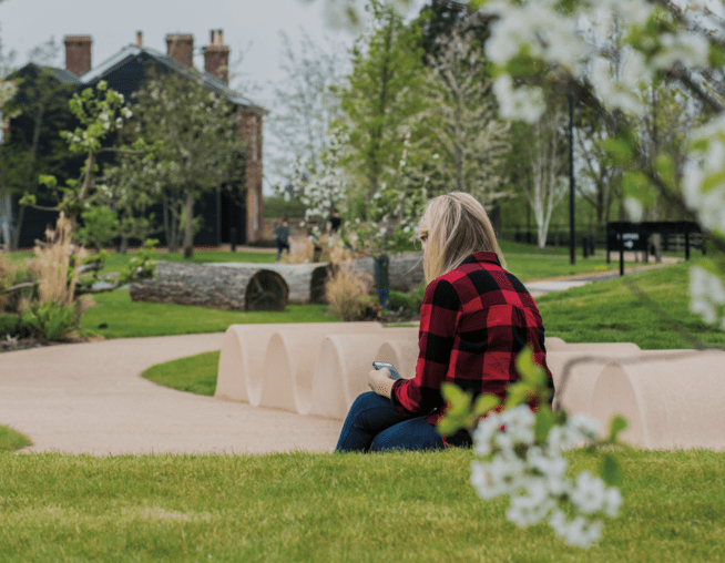 An adult sat in a park setting surrounded by greenery and blossoming trees.