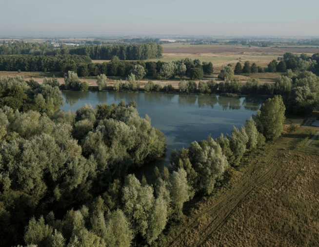 A photograph taken from a drone showing existing Waterbeach lake surrounded by mature trees.